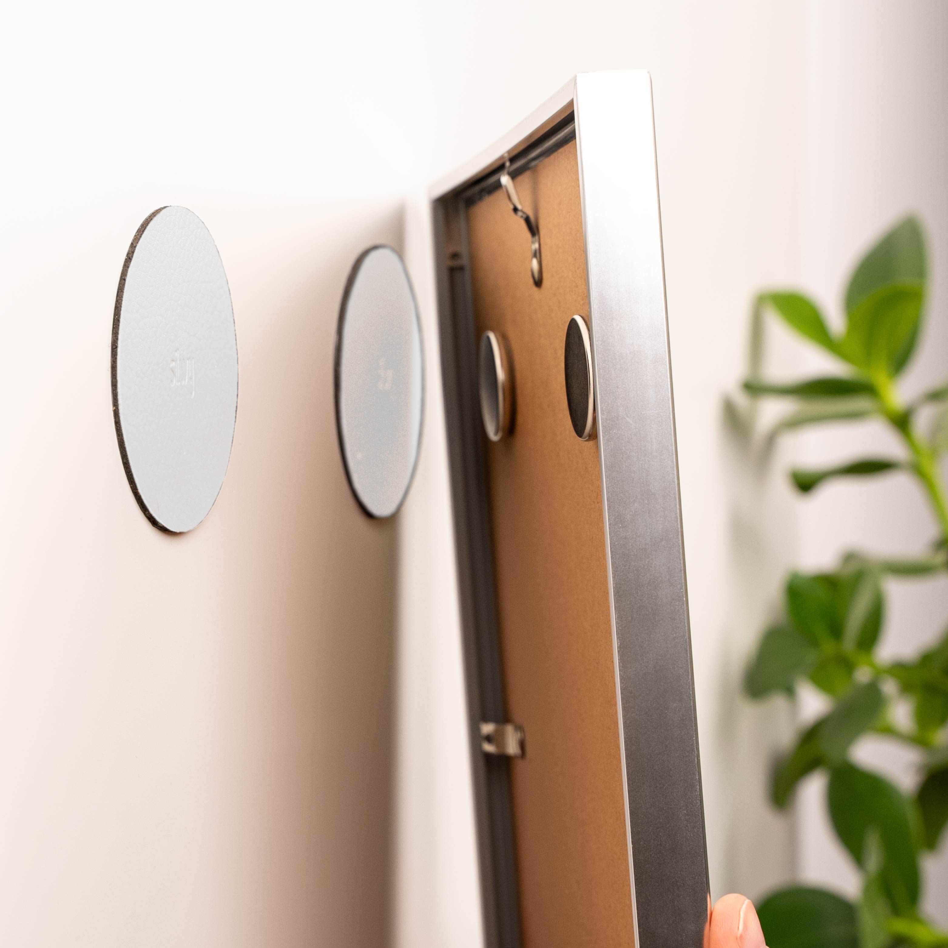 two round power magnets attached to a picture frame and two round Metal nano gel pads in white on the wall