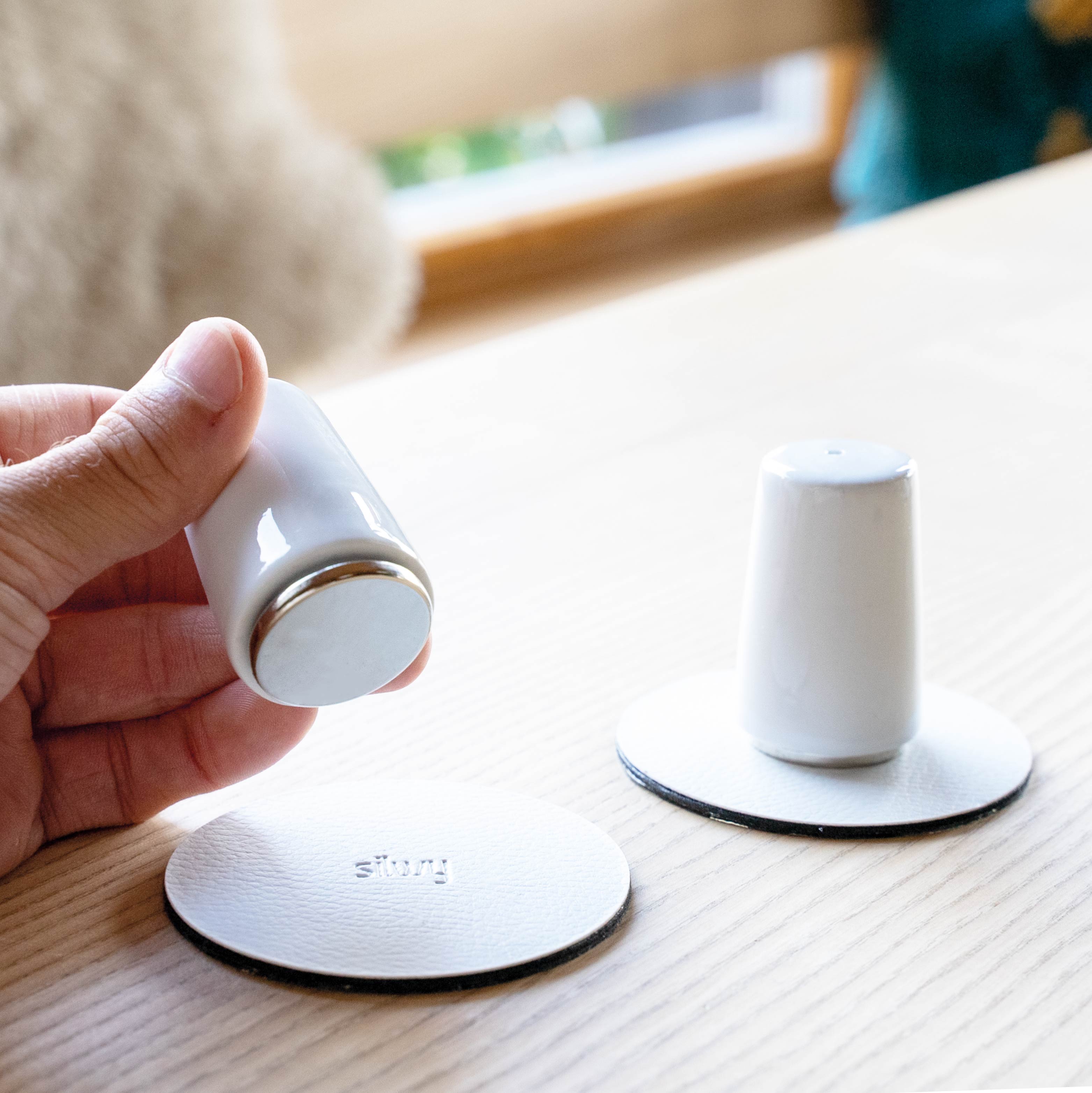 Two round power magnets attached to salt and pepper shakers on two white Metal nano gel pads