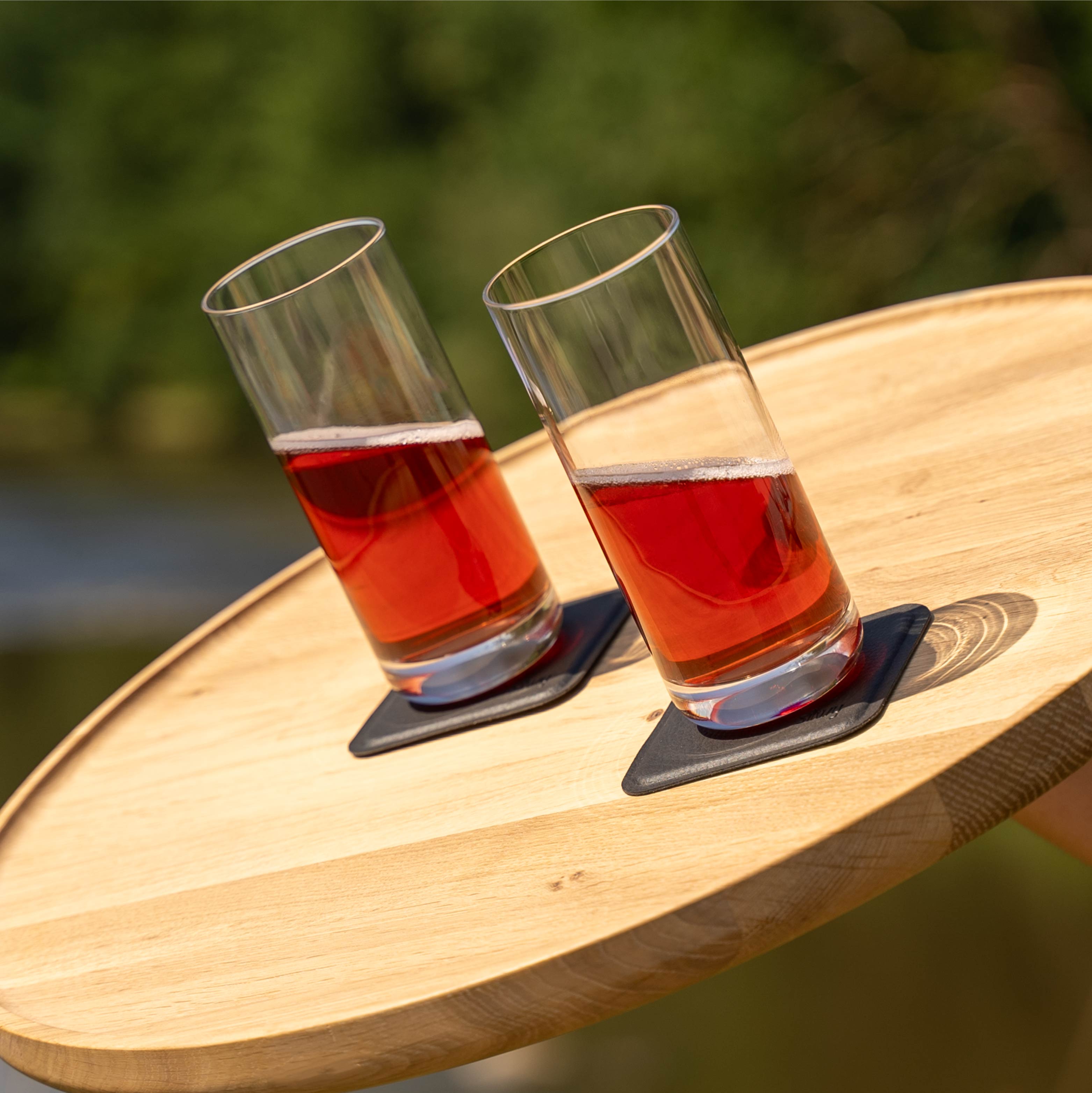 Bicchieri di cristallo magnetici Longdrink slim posizionati su cuscinetti, in posizione obliqua su un vassoio di legno