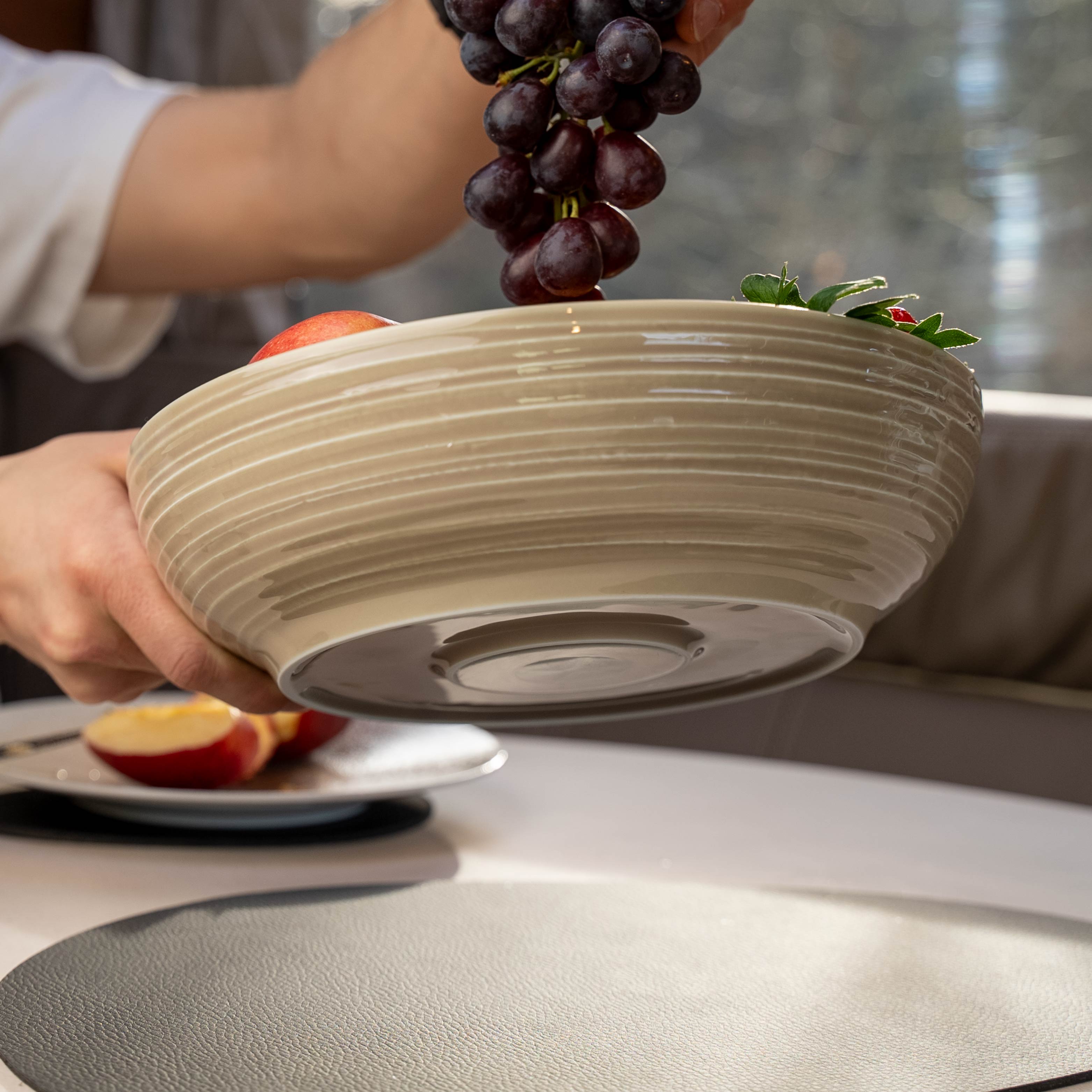Magnetic porcelain food bowl sand held in the air and integrated magnets in the base and metal mat on table as well as filled with grapes apples and strawberries 