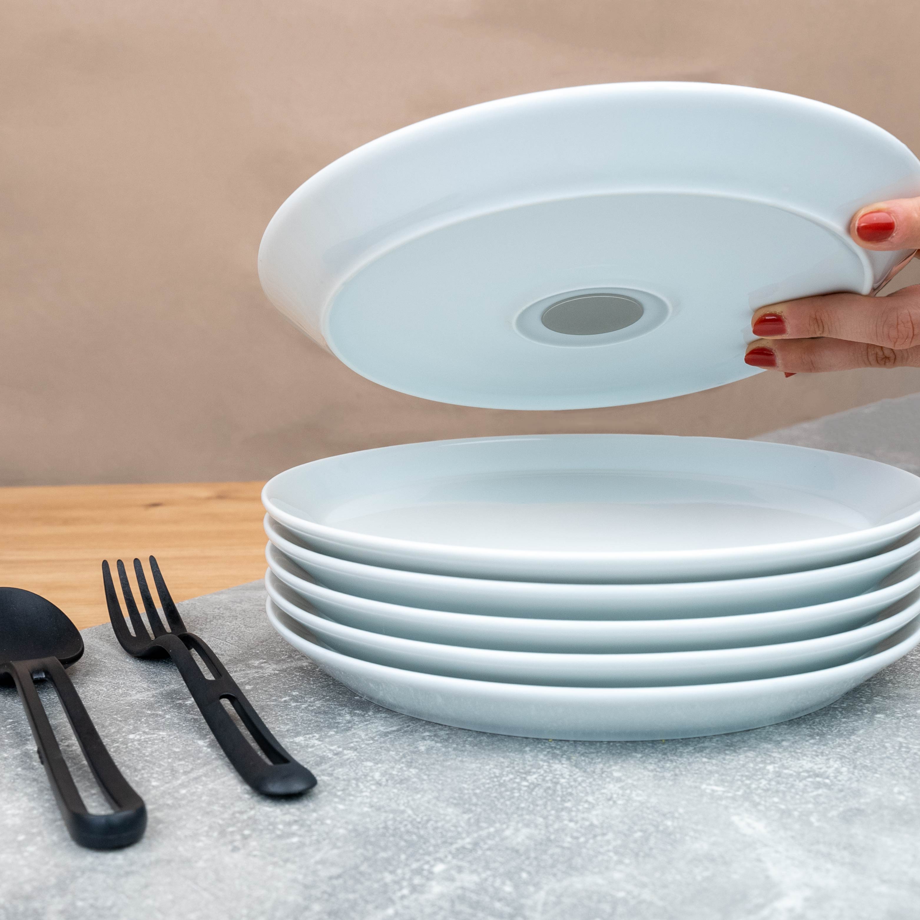 Magnetic porcelain plate with integrated magnet in the base stacked on a table and black Cutlery 