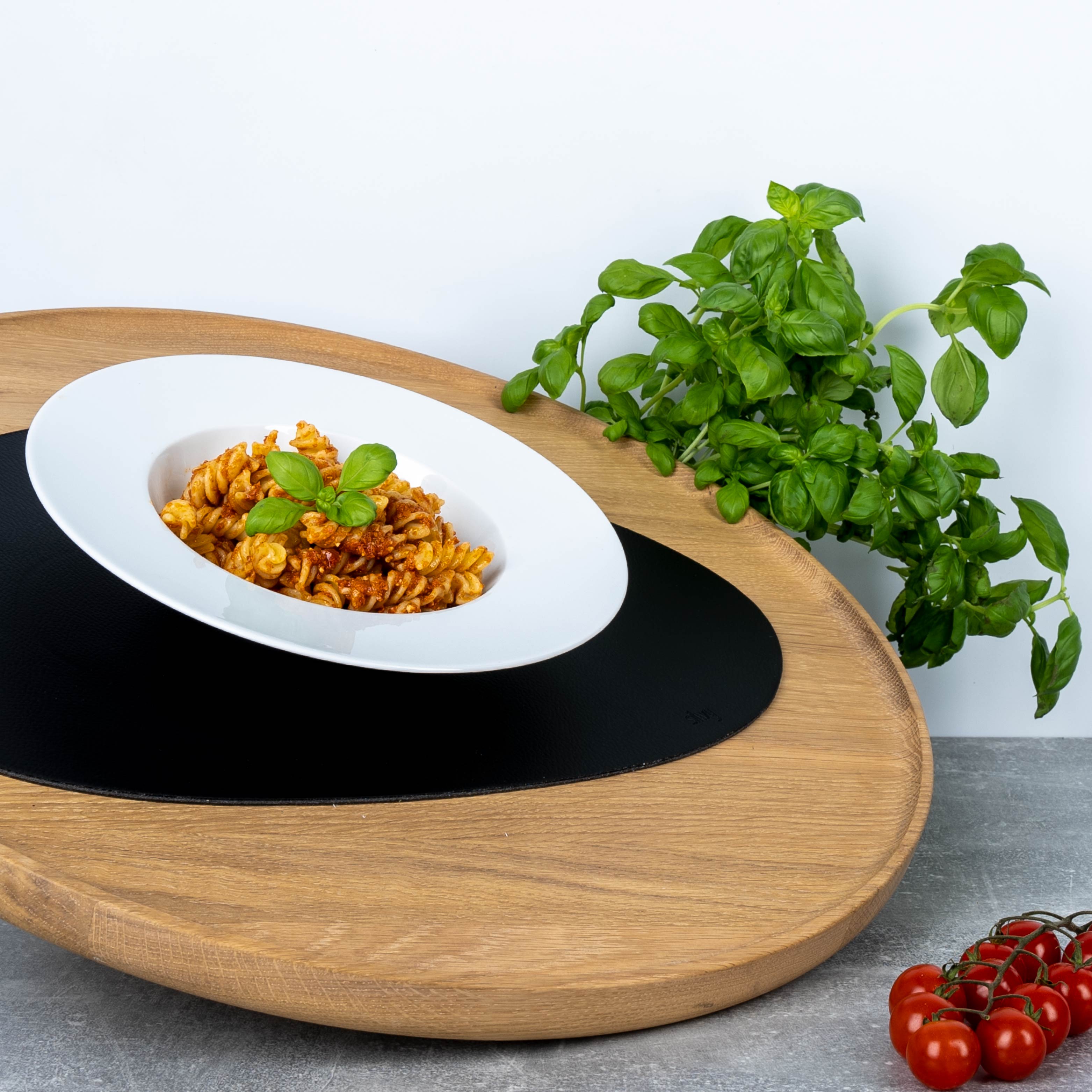 Plato gourmet de porcelana porcelana con pasta y albahaca sobre mantel individual en bandeja de madera 
