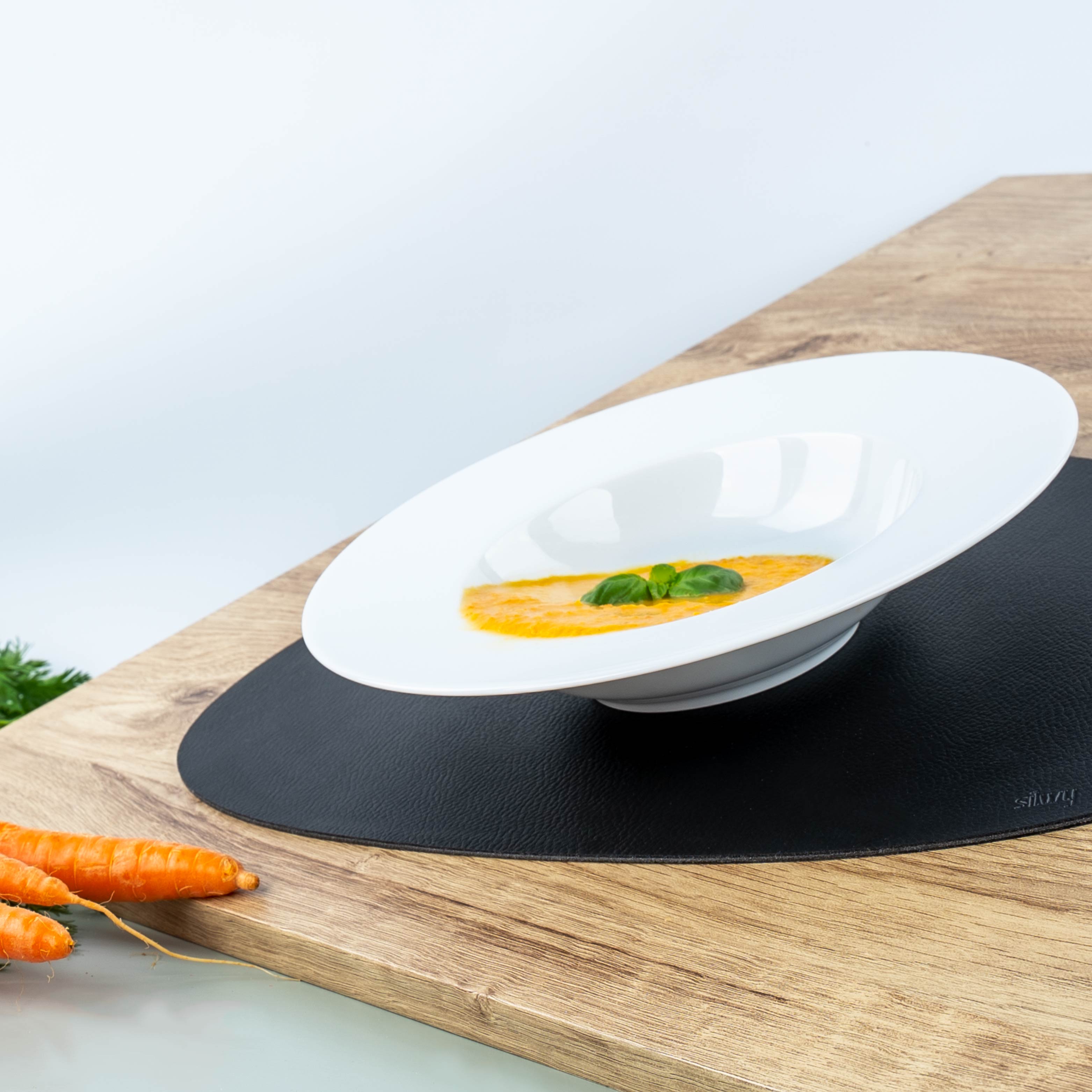 Plato gourmet de porcelana porcelana con sopa de zanahoria y albahaca sobre mantel individual 